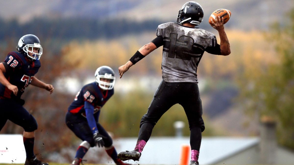 2 Football Players Running After Person Holding Football